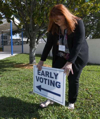 A woman sets up an 'early voting' sign on a lawn in front of a building