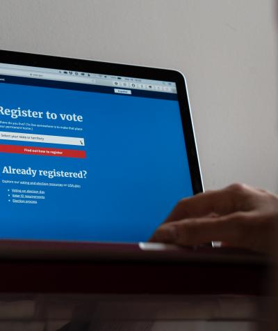 A close up of a laptop screen with a voter registration website and a person's hand on the keyboard