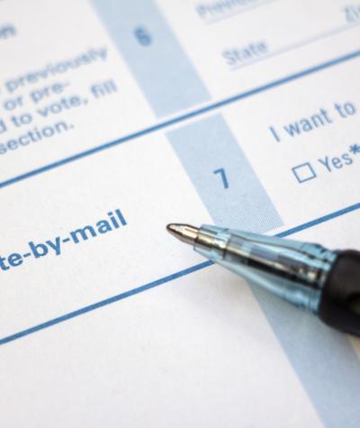 A voter registration form with text saying 'Vote by Mail' and a pen