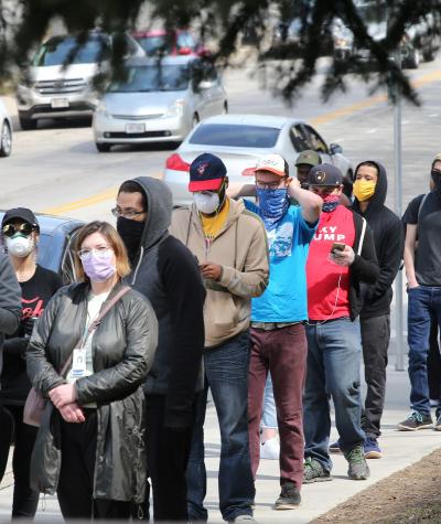 Line of people on the sidewalk wearing medical masks.