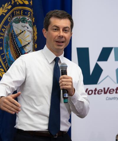 Pete Buttigieg speaking into a microphone in front of a VoteVets banner.