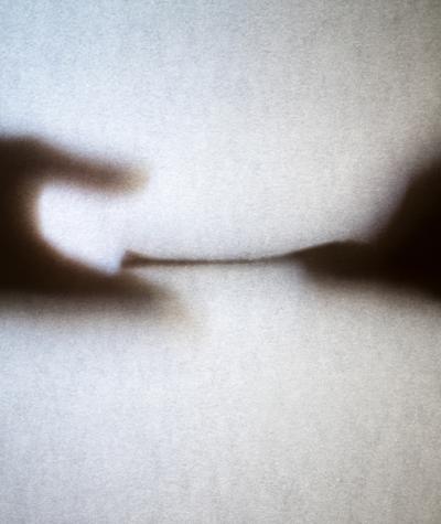 Two hands seen through frosted glass. One is passing a stack of what looks like money to another.