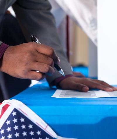 Hand of voter with a pen filling out a ballot