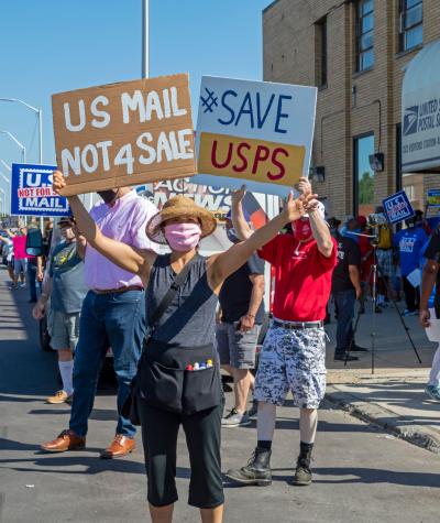 People wearing masks and holding up signs which say "Save USPS"