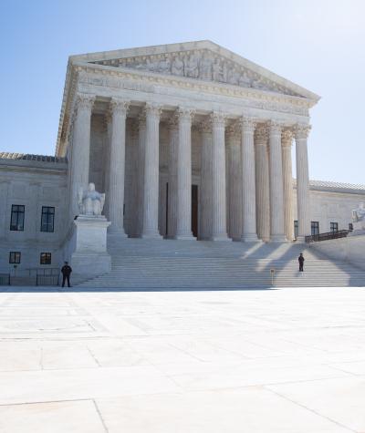 Wide shot of the Supreme Court with blue sky and the sun behind it