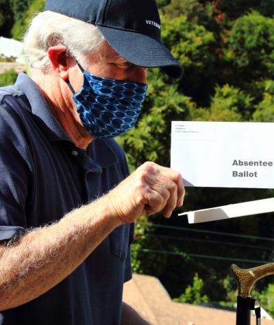 A man wearing a face mask putting an absentee ballot in the mail