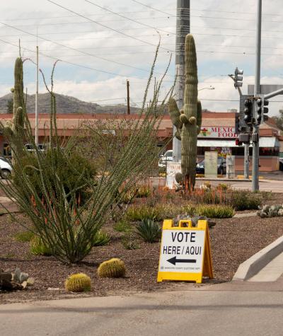 A "Vote Here/Aqui" sign on the side of the road with a cactus in the background