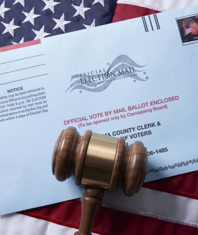 A gavel lies on top of a mail voting envelope on top of an American flag.