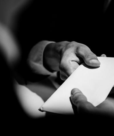 A black and white photo with one hand handing an envelope to another