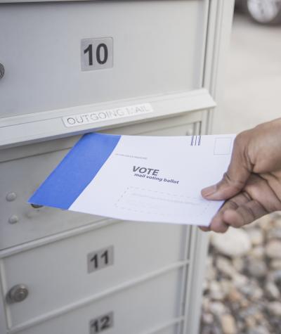 A person's hand putting an absentee ballot into a mail box