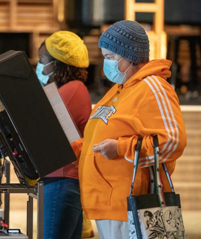 Two women wearing masks vote at electronic voting machines.