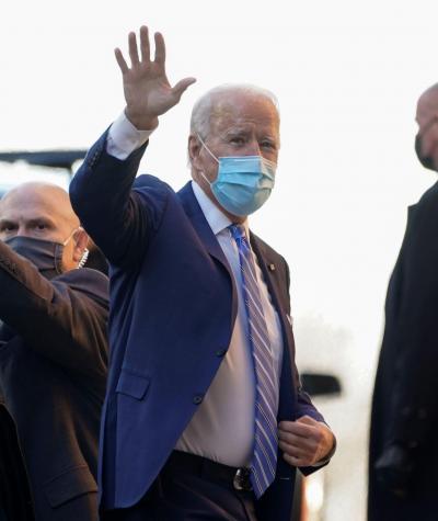 Joe Biden wearing a mask and waving as he gets out of a car