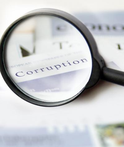 A magnifying glass held over a stack of newspapers with the word "corruption" in focus.