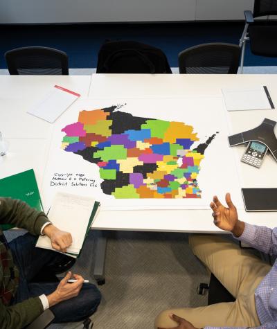 A top down view of a map of Wisconsin on a table with two people sitting next to it having a discussion