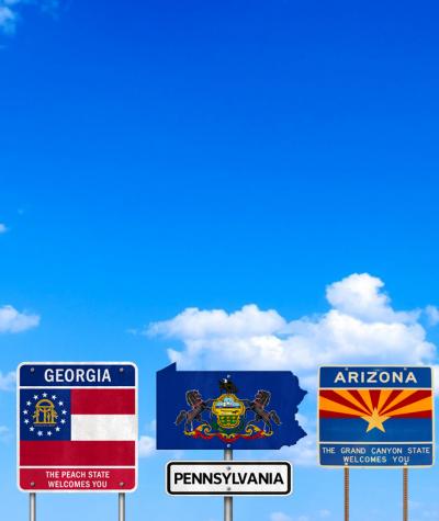 Road signs for the states Georgia, Pennsylvania and Arizona against a blue sky with clouds