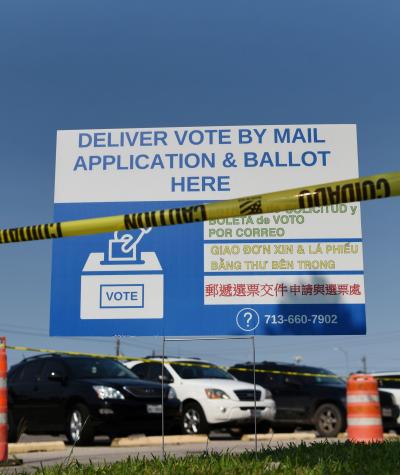 A sign that says "Deliver vote by mail application & ballot here" with caution tape in front of it.