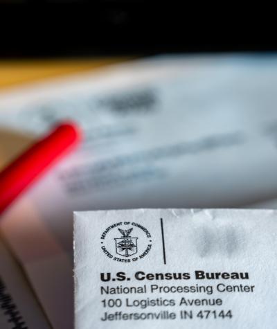 Close up of the return address on a census envelope with papers and a red pen out of focus in the background