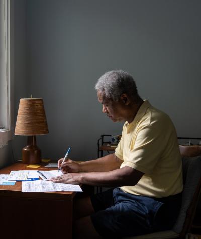 A man sitting at a desk in front of a window filling out a ballot.