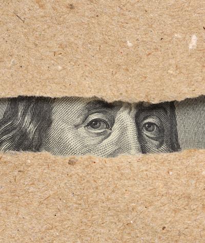 Benjamin Franklin's face on the one hundred dollar bill seen peeking out from behind two pieces of torn paper.