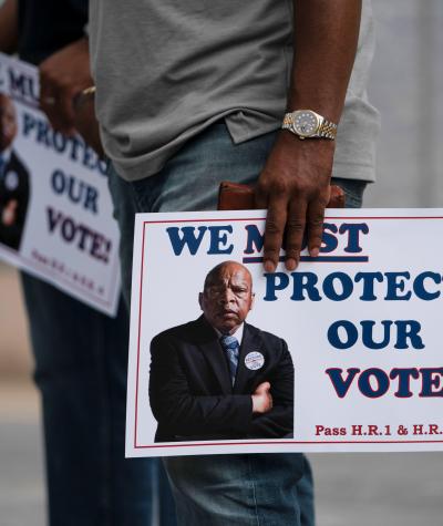 A person holds a sign with John Lewis's face on it which says, "We must protect our vote!"