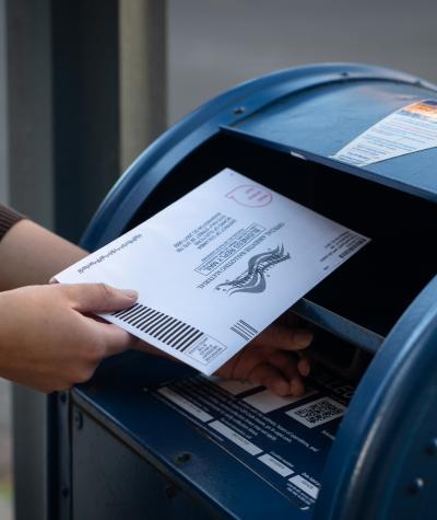 Close up of a woman's hands putting an envelope into a large blue mailbox.