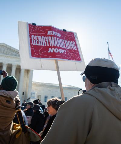 People in front of the Supreme Court holding signs that say "End gerrymandering now!"