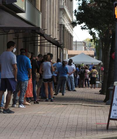 Voters stand in line on a sidewalk. There is a sign about where voters should park. 