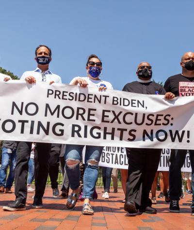 A row of people hold a sign which says, "President Biden, no more excuses, voting rights now!"