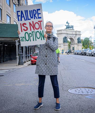A woman standing in the middle of the street holding a sign that says "Failure Is Not An Option".