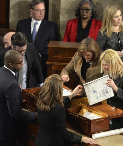 A group of people in suits, gathered around boxes, unsealing envelopes.