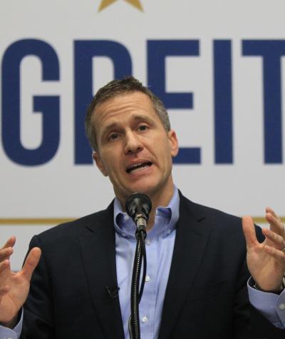 Eric Greitens giving a speech in front of a large sign that says "Greitens".