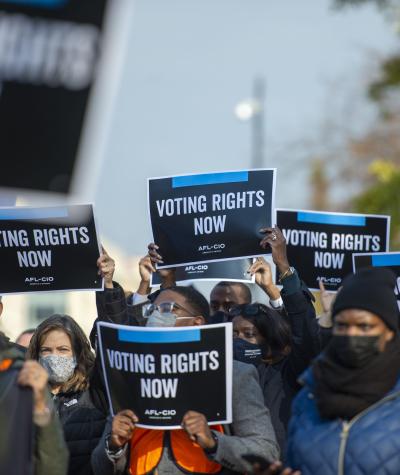 People wearing coats and hats hold signs that say "Voting rights now"