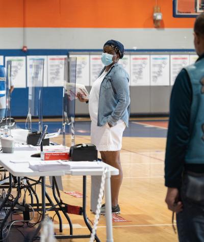 A women with a mask checks in at a polling place inside a school gym