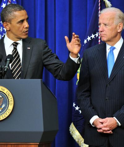 Barak Obama standing at a podium gesturing with Joe Biden standing to his right with his hands folded in front of him.