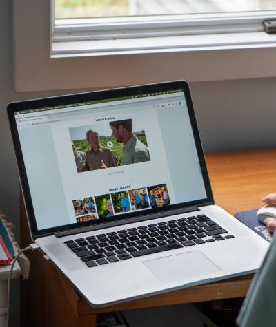 Over the shoulder shot of a woman looking at a laptop screen which is open to a web browser showing a page with videos and images.