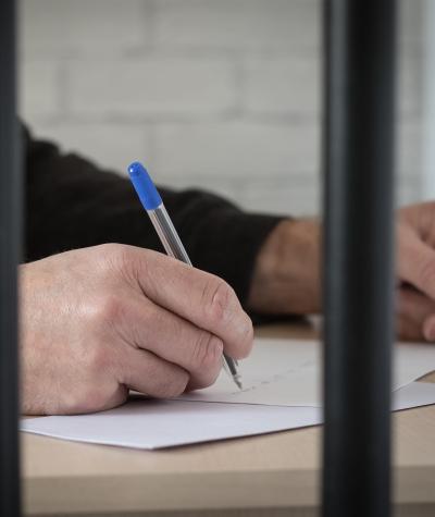 A man's hand holding a pen and writing behind bars