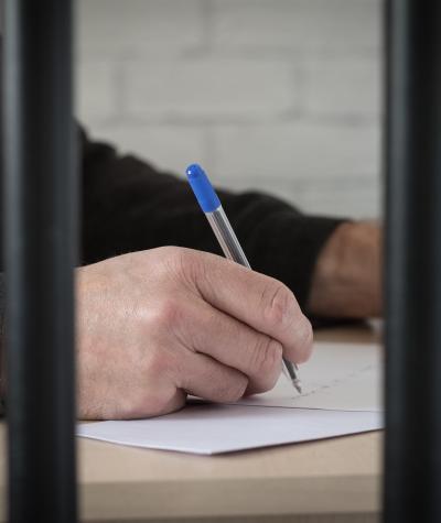 A man's hand holding a pen and writing behind bars.