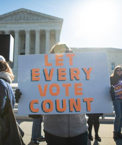 A woman holds a sign while standing outside the U.S. Supreme Court which reads "Let Every Vote Count"