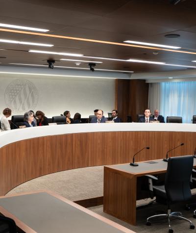 A long curved desk, behind which are sitting the FEC commissioners and their staff