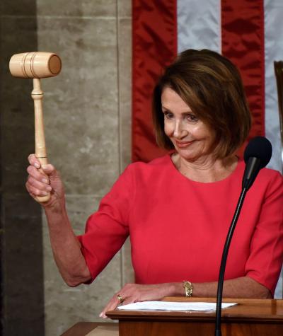 Nancy Pelosi standing at a podium raising a gavel and smiling