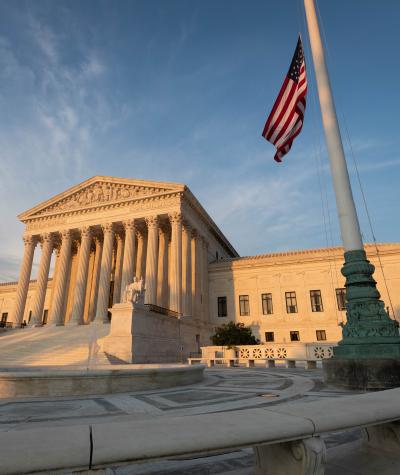 The U.S. Supreme Court in the late afternoon light with an American flag flying next to it.