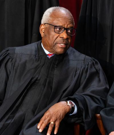 Clarence Thomas seated in black robes speaking with Chief Justice John Roberts