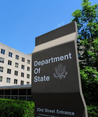 A sign saying "Department of State" in front of a plain concrete building with windows