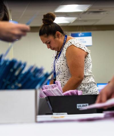A woman bends over a table with boxes of ballots