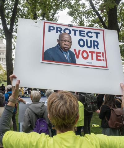 A person holds a sign featuring John Lewis, which says "Protect Our Vote" in front of the U.S. Capitol Building