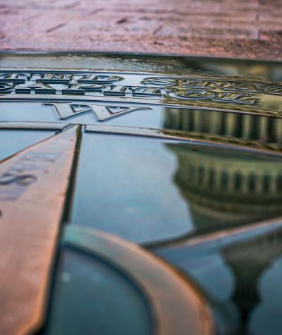 The dome of the U.S. Capitol Building reflected in a puddle on top of a compass rose.
