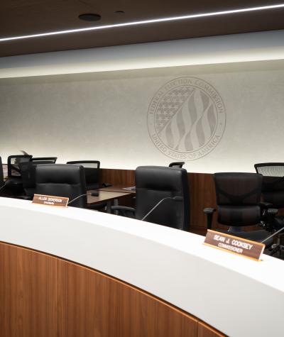 Chairs behind a desk with a large logo of the FEC on the wall behind them