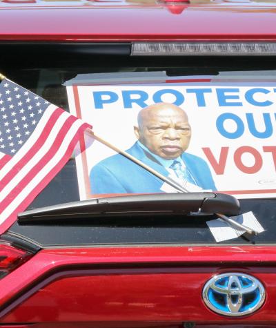 A poster of John Lewis that says "Protect Our Vote" on the back of a car windshield along with an American flag
