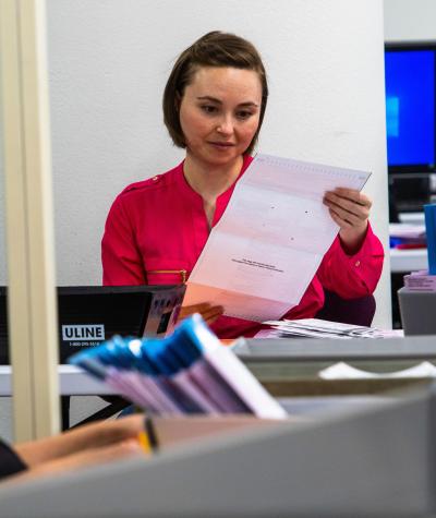 A woman seated at a desk looks over a ballot while another woman looks on