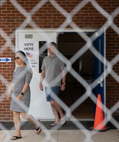A man and woman exiting a building through double doors seen through a chain link fence